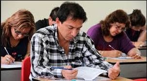 Docente mujer en aula, preparando ascenso en la escala magisterial